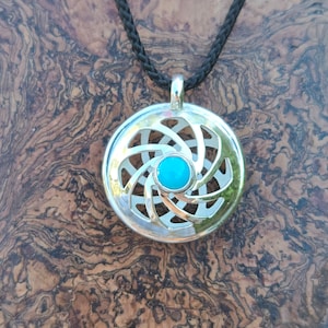 May include: Silver pendant necklace with a turquoise stone in the center. The pendant is a circular design with a spiral pattern.