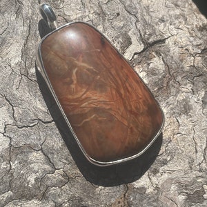 May include: A brown and white patterned stone pendant with a silver setting. The pendant is shaped like a teardrop and has a smooth, polished surface.