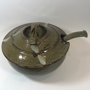May include: A green ceramic soup tureen with a lid and a ladle. The tureen is decorated with white dragonfly designs.