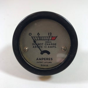 May include: A black and silver automotive charging gauge with a needle pointing to the 'normal' range. The gauge reads 'DO NOT CHARGE ABOVE 13 AMPS.' and 'AMPERES' with the patent number '1,970,889' and '244-A'.