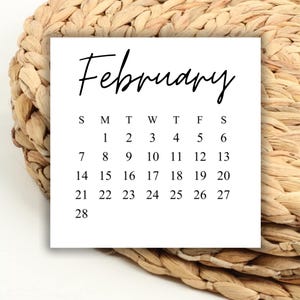 Könnte beinhalten: Ein weißer Kalender mit dem Monat Februar. Der Kalender zeigt die Wochentage und die Daten für den Monat. Der Kalender liegt auf einem gewebten Hintergrund.