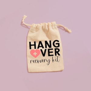 Può includere: Una borsa di cotone bianco con coulisse, con il testo "HANGOVER recovery kit" in lettere nere. Un cuore rosa con una croce bianca è al centro del testo.