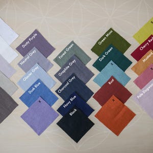 May include: A collection of square fabric swatches arranged in a grid, featuring a wide variety of colors including white, off-white, dusty purple, neutral grey, natural linen, forest green, moss, cherry red, mustard, rust, navy blue, and black.