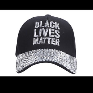 May include: A black baseball cap with a silver sequined brim. The front of the cap features the words "Black Lives Matter" in silver rhinestones.