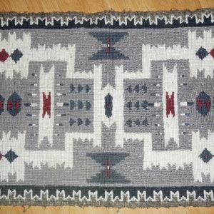 Könnte beinhalten: Ein geometrischer Teppich in Grau, Weiß, Rot und Blau mit einem Fransenrand.