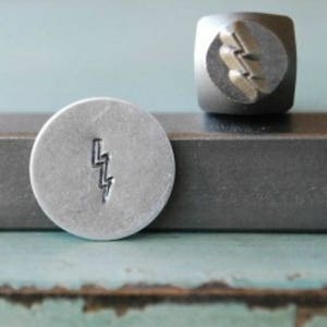 May include: A silver metal stamp with a lightning bolt design. The stamp is used to create impressions in metal.