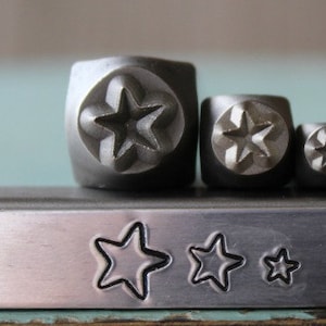 May include: Set of five metal star-shaped stamps, arranged in size order from largest to smallest. The stamps are made of a silver-colored metal and have a smooth, polished finish.