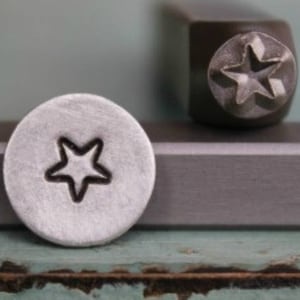 May include: A silver metal stamp with a five-pointed star design. The stamp is used to create impressions on metal.