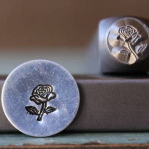 May include: A close-up of a metal stamp with a rose design. The stamp is used to create impressions on metal.