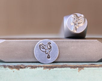 May include: Two metal stamps with a design of a saddle. The stamps are silver in color and have a circular shape. The stamps are on a wooden surface.