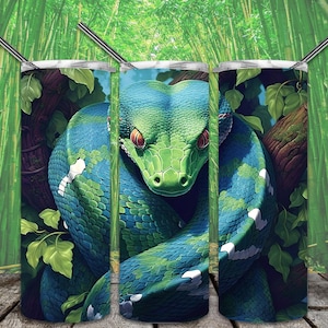 Op de afbeelding: Drie roestvrijstalen bekers met een groene slang die om een ​​boomtak gewikkeld is. De slang heeft blauwe en groene schubben en rode ogen. De achtergrond is een groen bamboebos.