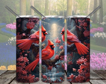 Op de afbeelding: Drie rode kardinaalsvogels zitten op takken met roze bloesems in een donkere bossetting. De kardinaalsvogels staan in een driehoekige formatie met een maan op de achtergrond. De afbeelding is voor een tumbler.