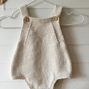 May include: A cream knitted baby onesie with a heart-shaped design and wooden buttons.