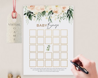 May include: A white Baby Bingo game card with gold grid lines, floral accents, and the text "BABY Bingo." The card includes instructions and is decorated with watercolor flowers. A hand is holding a pen, ready to mark the squares.