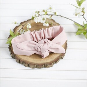 May include: A pink fabric headband tied in a bow knot. The headband is on a wooden slice.