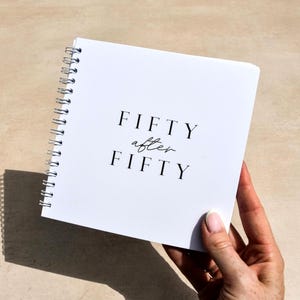May include: A square white spiral-bound notebook with the text FIFTY after FIFTY printed in black on the front cover. The notebook features a clean design with a simple serif font for the word FIFTY and a cursive script for the word after.