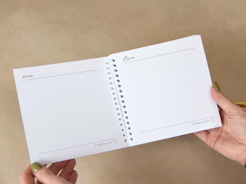 May include: Open spiral-bound notebook with blank white pages. The left page has the word "one" and a horizontal line. The right page has the word "two" and a horizontal line. The word "COMPLETED" is at the bottom of each page.