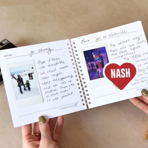 May include: A spiral-bound travel journal with handwritten notes and photos. One page features a photo of people skiing with the text "go skiing" and "Alpe d'Huez". The other page has a photo with the text "go to Nashville" and a heart-shaped sticker that says "NASH".