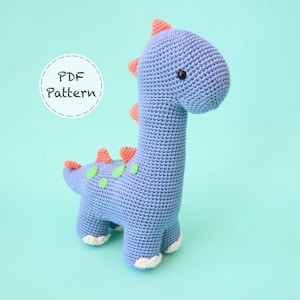 May include: A crocheted blue dinosaur toy with green and orange accents. The dinosaur has a long neck and a small head with black eyes. The toy is sitting on a light blue background. PDF Pattern.