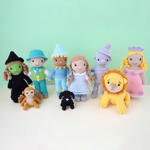 May include: A collection of handmade crochet dolls depicting characters from The Wizard of Oz. The dolls include Dorothy, the Scarecrow, the Tin Man, the Cowardly Lion, the Wicked Witch, Glinda, and a monkey and a black dog. Each doll is brightly colored.