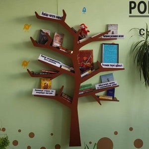 May include: A brown wooden bookshelf shaped like a tree with books on the shelves. The shelves are labelled with phrases in a foreign language, such as "Why read books?" and "Reading develops the brain".