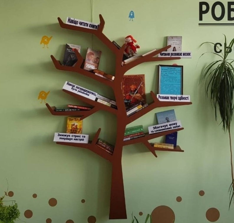 May include: A brown wooden bookshelf shaped like a tree with books on the shelves. The shelves are labelled with phrases in a foreign language, such as "Why read books?" and "Reading develops the brain".