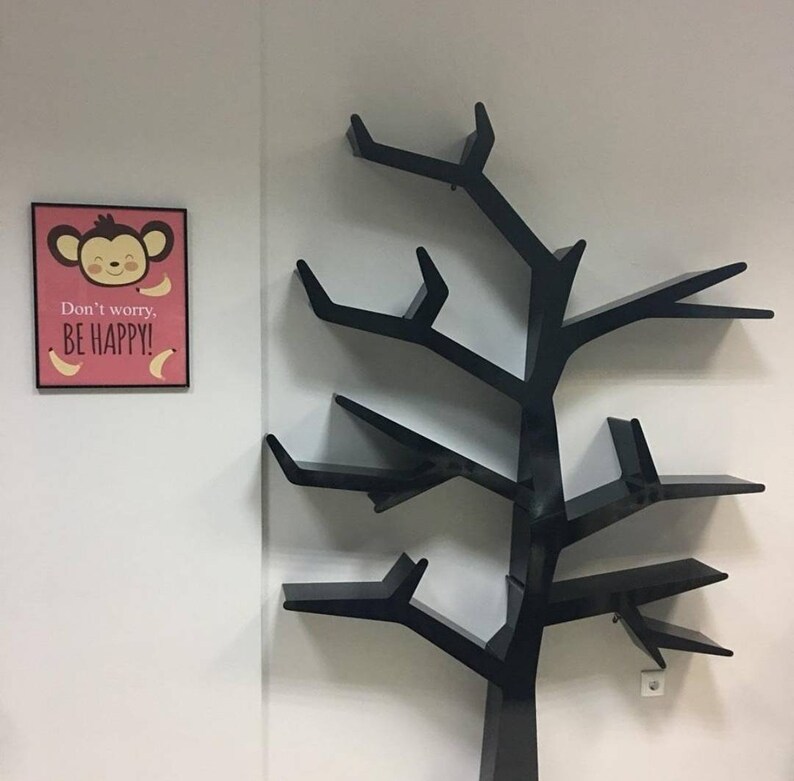 May include: Black tree-shaped bookshelf with multiple shelves. A pink framed poster with a cartoon monkey and the text "Don't worry, BE HAPPY!" is on the wall behind the bookshelf.