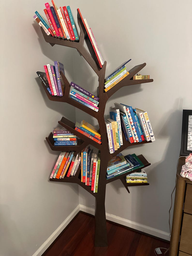May include: A dark brown, tree-shaped bookshelf filled with colorful books. The bookshelf is made of wood and has multiple branches that serve as shelves. The books are of various sizes and colors, creating a visually appealing display. The bookshelf is placed in a corner.