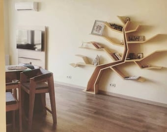 Puede incluir: Una estantería de madera con forma de árbol con múltiples ramas y estantes. La estantería está montada en una pared de una sala de estar con un televisor y una mesa con sillas en primer plano.