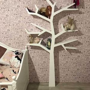 May include: White tree-shaped bookshelf with multiple shelves, decorated with stuffed animals and dolls. The bookshelf is against a pink wall with a black and white dog pattern.