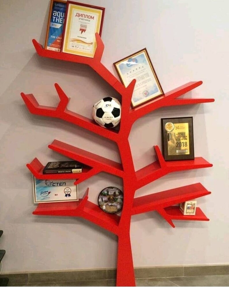 May include: Red tree-shaped bookshelf with multiple shelves and branches. The shelves are decorated with books, diplomas, a football, and other items.