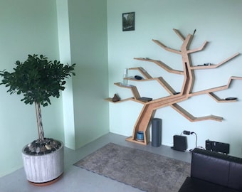 Puede incluir: Una estantería de madera con forma de árbol con múltiples ramas y estantes. La estantería está montada en una pared de color verde claro. Una planta en maceta se encuentra en primer plano.