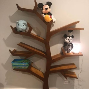 May include: A wooden tree-shaped bookshelf with multiple shelves. The shelves are decorated with a blue piggy bank, two Mickey Mouse plush toys, and a small lamp.