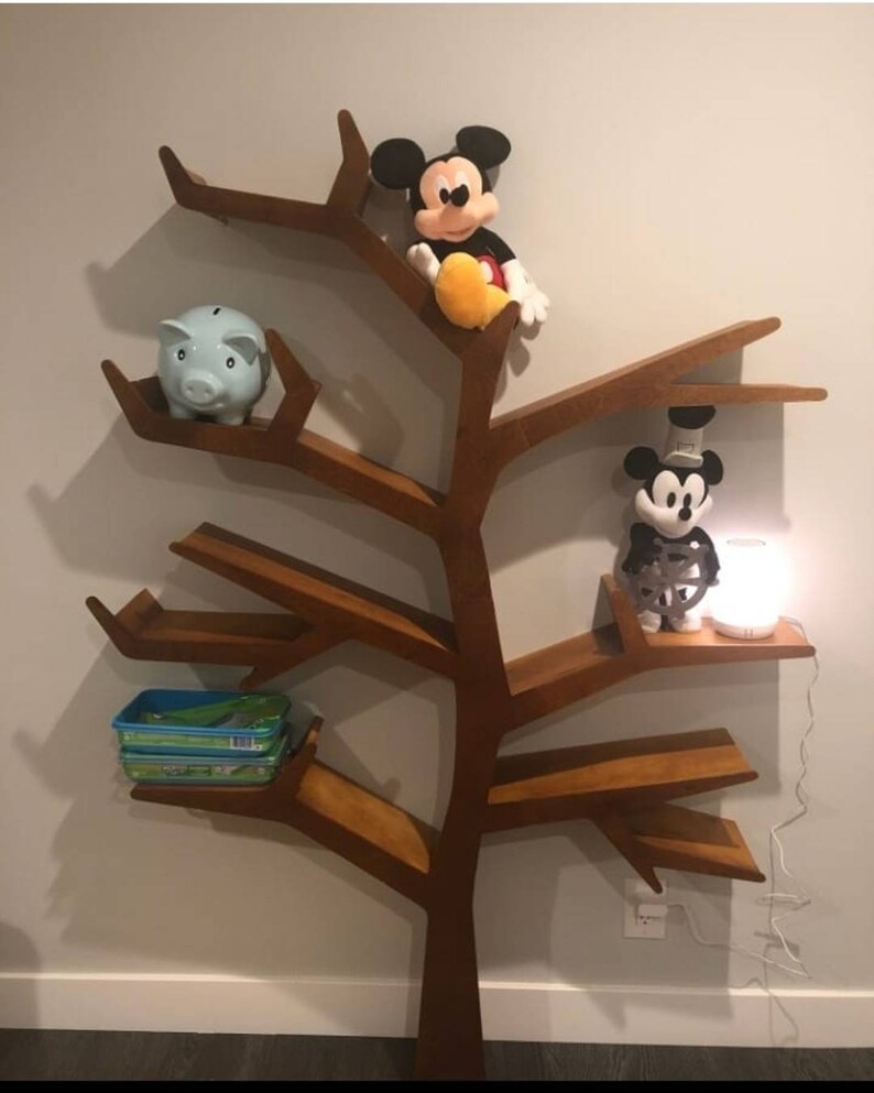 May include: A wooden tree-shaped bookshelf with multiple shelves. The shelves are decorated with a blue piggy bank, two Mickey Mouse plush toys, and a small lamp.