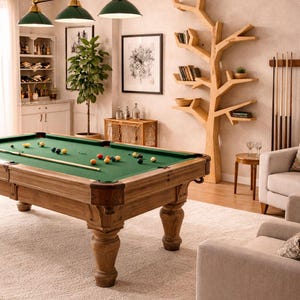 May include: A well-lit game room featuring a pool table with a green felt surface and wooden frame. The room includes a tree-shaped bookshelf, framed artwork, and a cream-colored rug. Overhead, three green and gold pendant lights illuminate the scene.