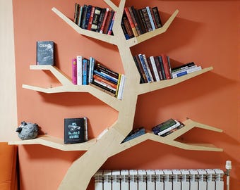 Puede incluir: Estantería con forma de árbol de madera clara, montada en una pared naranja. Las baldas contienen una variedad de libros. Un pequeño objeto decorativo gris se encuentra en una balda. Un radiador blanco se encuentra debajo.