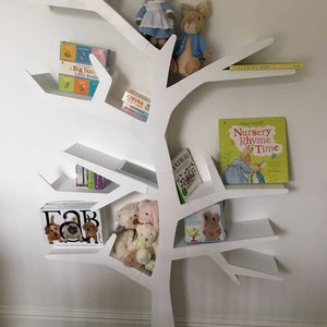 May include: White tree-shaped bookshelf with multiple shelves, featuring stuffed animals, children's books, and a tablet. The books include titles like "Welcome to the World", "A Big Box of Little Books", "Nursery Rhyme Time", and "Lavendern Blue".