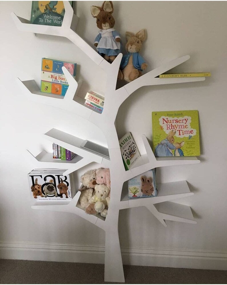May include: White tree-shaped bookshelf with multiple shelves, featuring stuffed animals, children's books, and a tablet. The books include titles like "Welcome to the World", "A Big Box of Little Books", "Nursery Rhyme Time", and "Lavendern Blue".