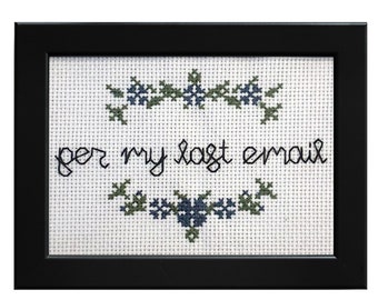 May include: A framed cross-stitch with a white background and green and blue floral embroidery. The text "per my last email" is stitched in black thread.