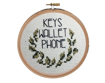 May include: A white embroidery hoop with a green leafy wreath surrounding the text "KEYS WALLET PHONE".