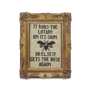 May include: A framed cross-stitch with a black and white moth and the text "IT RUBS THE LOTION ON ITS SKIN OR ELSE IT GETS THE HOSE AGAIN".