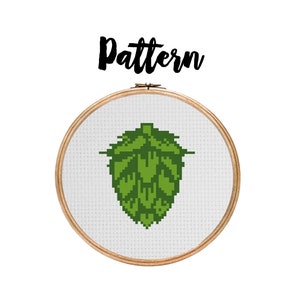 May include: A green and white cross-stitch pattern of a hop cone, a key ingredient in beer brewing, displayed in a wooden embroidery hoop.
