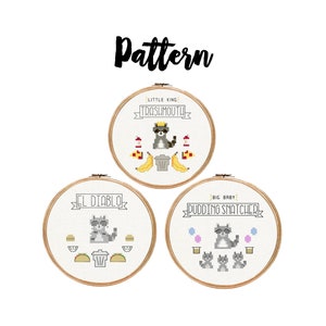 May include: Three cross-stitch patterns in wooden hoops featuring raccoons with text. The top hoop says "Little King Trashmouth!" with a raccoon wearing sunglasses and a crown. The other hoops say "El Diablo" and "Big Baby Pudding Snatcher". The word "Pattern" is above.