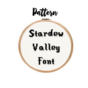 May include: A wooden embroidery hoop with white fabric stretched across it. The fabric has black pixelated text that reads "Stardew Valley Font" and the word "Pattern" is written in black cursive above the hoop.