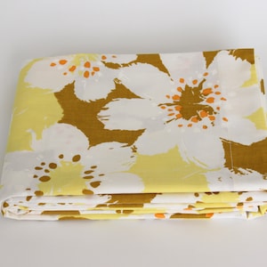 May include: A folded fabric with a floral pattern in shades of white, yellow, and brown. The fabric features large, stylized flowers with orange accents.