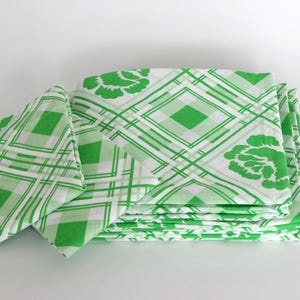 May include: Folded fabric with a green and white geometric pattern. The design features diamond shapes, lines, and floral accents. The fabric is a vibrant green colour.