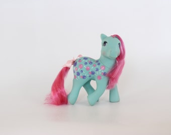 Puede incluir: Un juguete My Little Pony azul claro con pelo rosa y un diseño de piruletas moradas y rosas en su cuerpo.