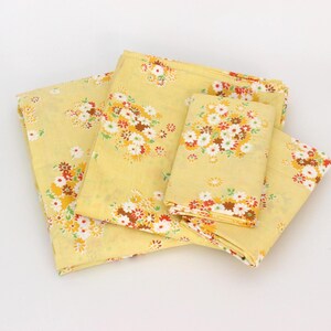 Peut inclure: Ensemble de pièces de tissu jaune à motifs floraux, dont un grand carré, un carré plus petit et deux pièces rectangulaires. Le motif floral présente des fleurs blanches, marron, orange et rouges. Le tissu est plié et disposé sur une surface blanche.