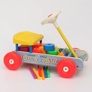 Peut inclure: Un chariot à jouets vintage Fisher-Price Creative Coaster avec un siège jaune, des roues bleues et blanches et une poignée jaune. Le chariot est rempli de blocs colorés et comprend un ensemble de bâtonnets arc-en-ciel.