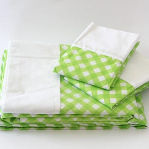 Peut inclure: Un ensemble de literie plié avec des taies d'oreiller et des draps à carreaux vichy blancs et verts. Les draps sont empilés, avec les taies d'oreiller soigneusement disposées dessus. La palette de couleurs est vive et gaie.